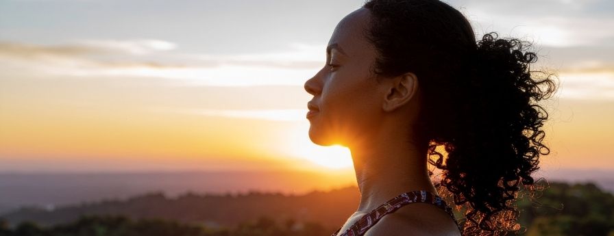 Una donna guarda in alto verso il sole, circondata da un paesaggio naturale