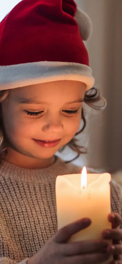 bambina con cappello di babbo natale che guarda una candela accesa