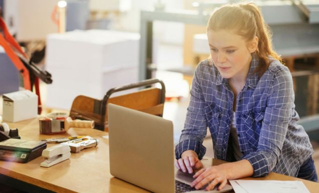 Una donna utilizza un laptop, immersa nel suo lavoro tra attrezzature industriali