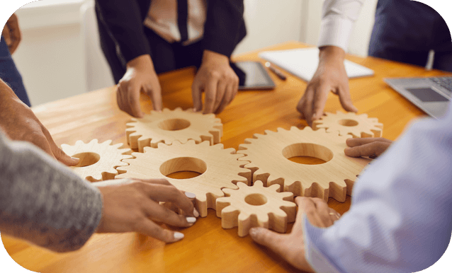 Un gruppo di professionisti tiene insieme ingranaggi di legno, simboleggiando collaborazione e lavoro di squadra.