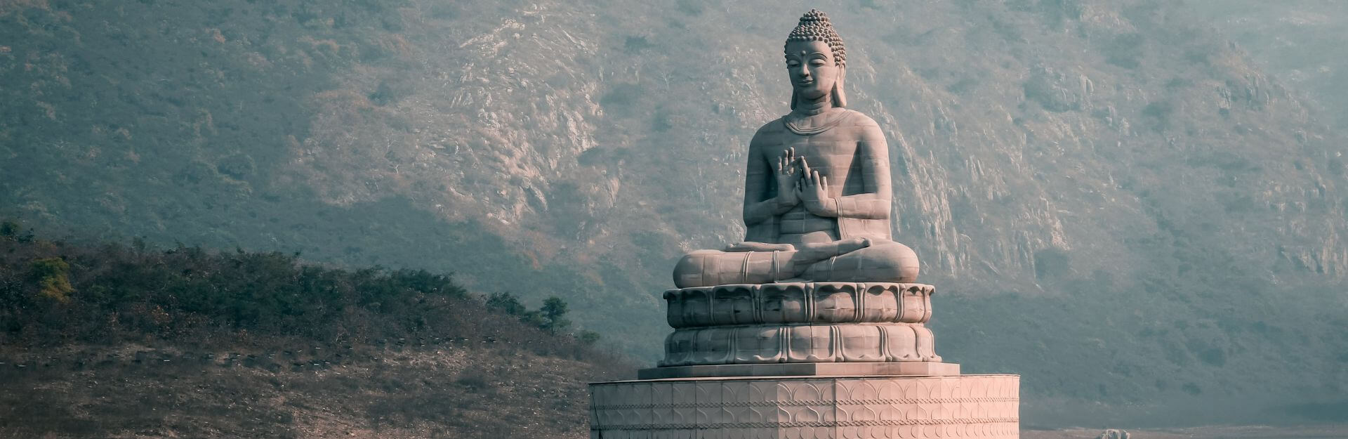 Buddha in meditazione su un ledge di pietra, con montagne sullo sfondo
