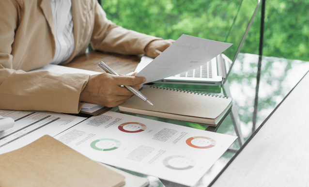 Persona concentrata a una scrivania, utilizzando un laptop e circondata da documenti