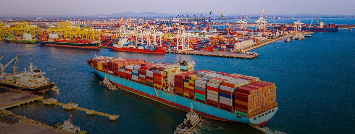 Nave cargo di grandi dimensioni attraccata in un porto, circondata da container e attrezzature portuali.