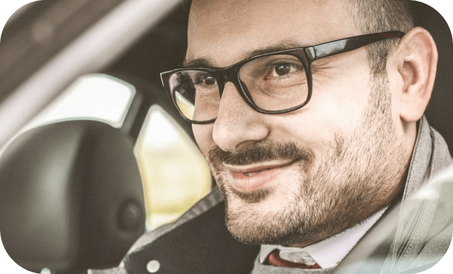 Un uomo in cravatta e occhiali sorride mentre si trova in un'auto.
