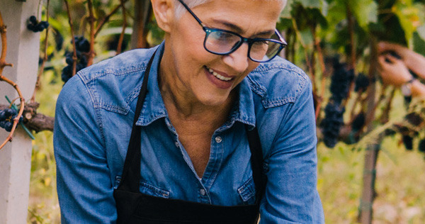 L'immagine mostra una donna sorridente mentre lavora in un vigneto