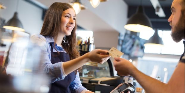 Un uomo sta consegnando una carta di credito ad una barista, simbolo di un acquisto o pagamento.