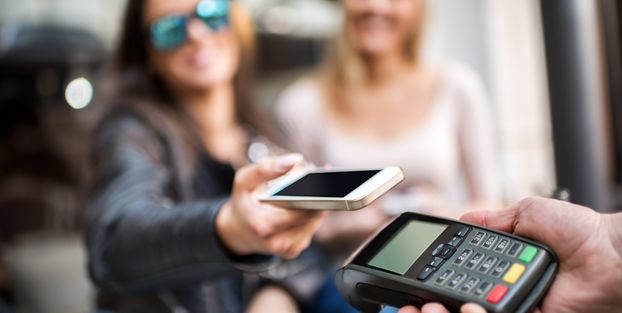 Donna che tiene in mano un cellulare e una carta di credito all'interno, simbolo di servizi di pagamento alternativi al contante.