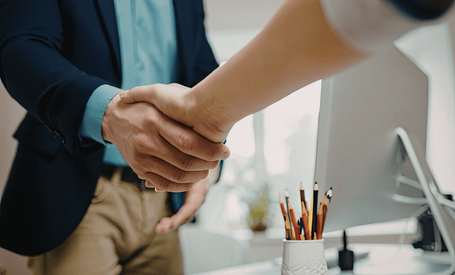 Due uomini si stringono la mano davanti a una scrivania.
