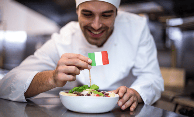Cuoco che posiziona una bandierina italiana sopra un piatto di pasta