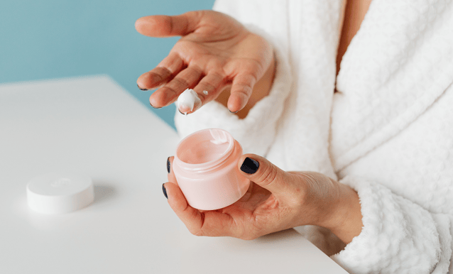 Una donna in un accappatoio tiene un barattolo di crema, pronta ad applicarlo sulla pelle.