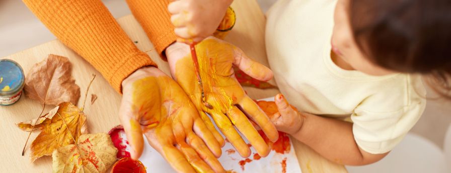 Mani di genitore dipinte da colore a tempera giallo per mano di una bambina
