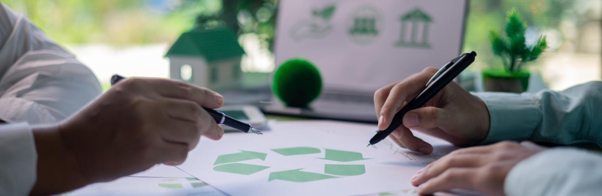sfondo verde e computer con immagini proiettate a tema sostenibilità, in primo piano due figure che stanno per firmare un contratto