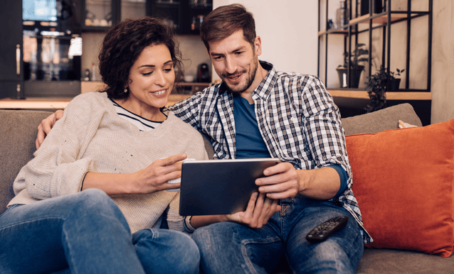 un uomo e una donna seduti sul divano hanno un tablet in mano che gestiscono la loro pratica di mutuo da remoto