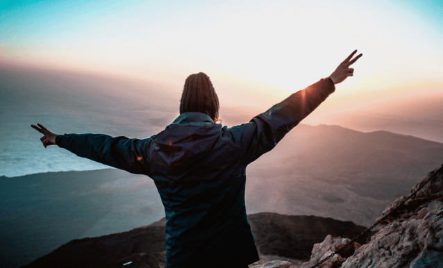 Una persona in cima a una montagna con le braccia aperte, esprimendo gioia e libertà.