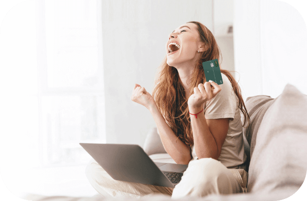 Ragazza che urla in maniera euforica con i mano la sua carta di credito e il computer di fronte perché è riuscita a spostare il massimale della sua carta sul conto