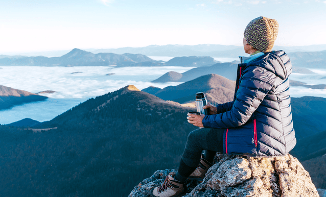 Una donna seduta in cima a una montagna mentre ammira il panorama.