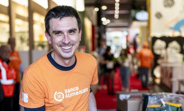 Operatore del banco alimentare in camicia arancione, sorridente, durante un evento di distribuzione alimentare.