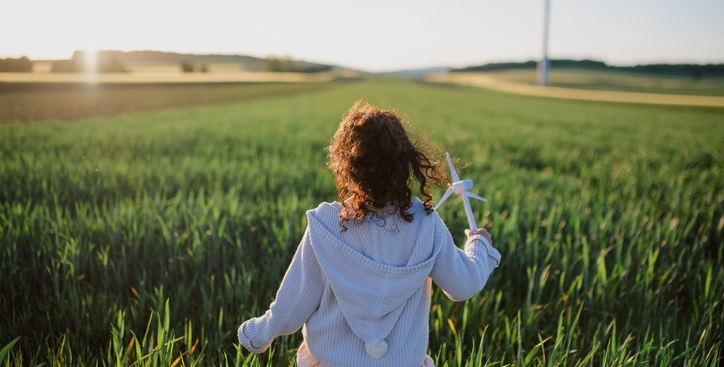 bambina che corre tra i campi tenendo in mano una pala eolica in miniatura