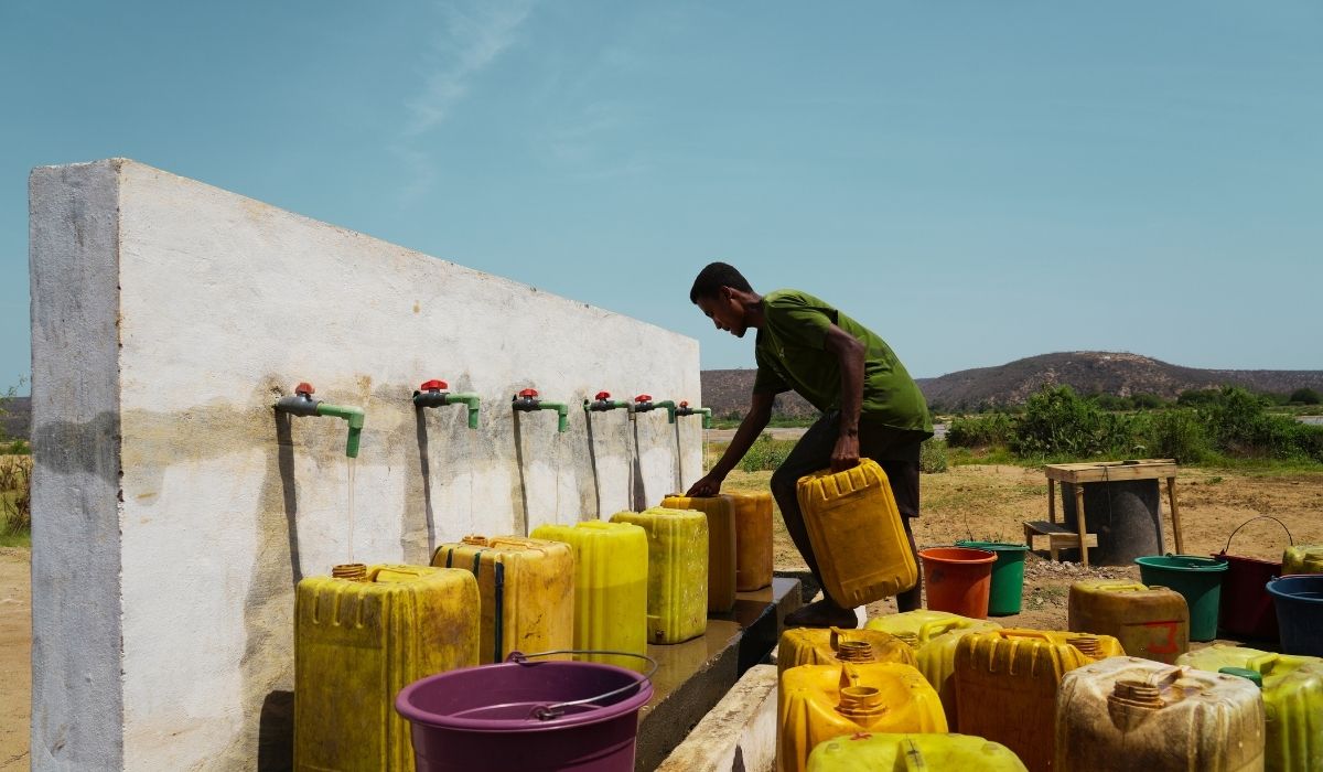 Uomo riempie un secchio d'acqua da un serbatoio in un territorio arido