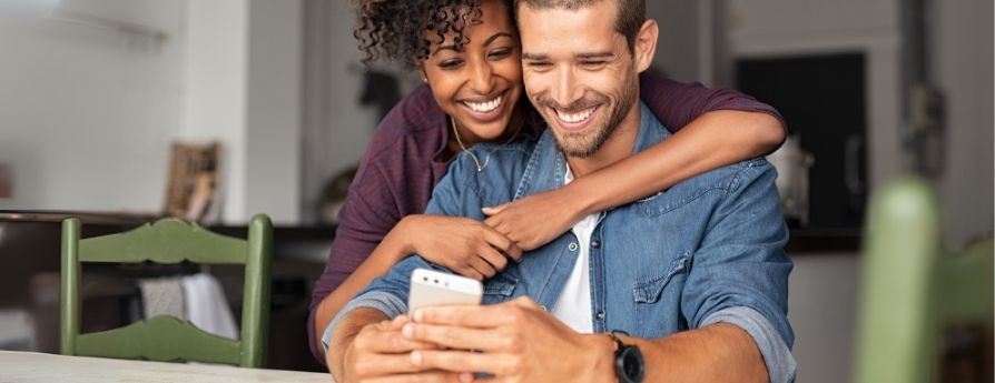 ragazza che abbraccia un ragazzo mentre sorridono guardando il cellulare