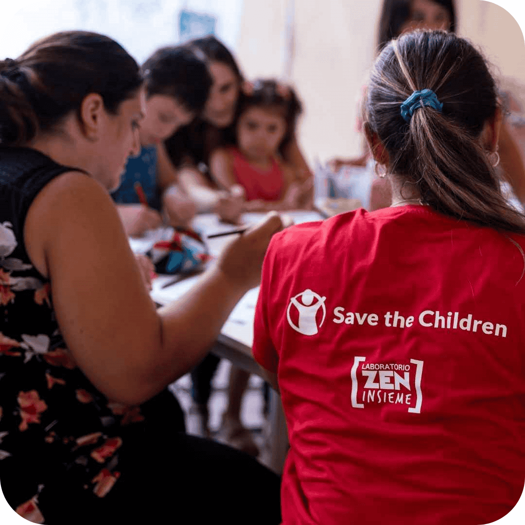 operatrice di save the children seduta al tavolo con mamme e bambini che disegnano